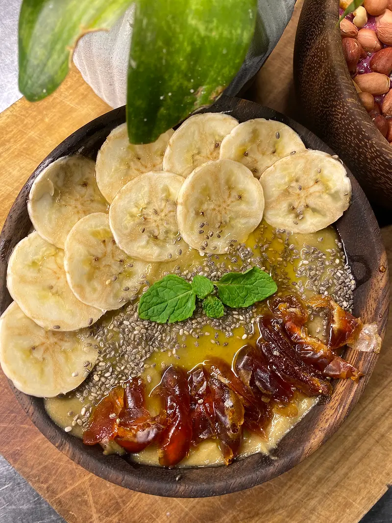 Smoothie bowl topped with sliced banana, dates, chia seeds, honey and a sprig of mint