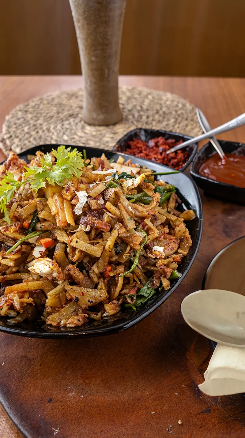 A plate of chicken kottu with chopped vegetables and chilli