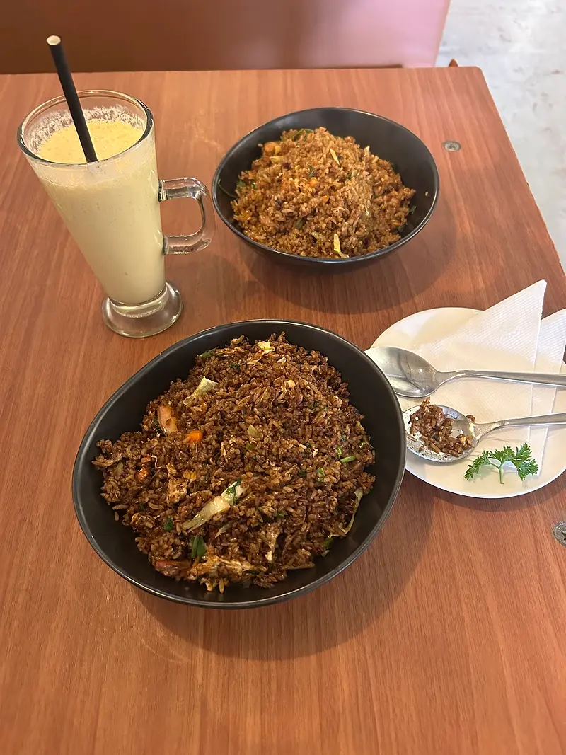 Two bowls of fried rice with a tall mango lassi on a wooden table