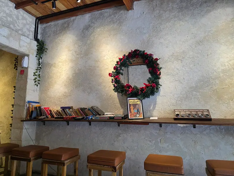 Bookshelf and leather bar stools along the textured plaster wall, with a wreath above