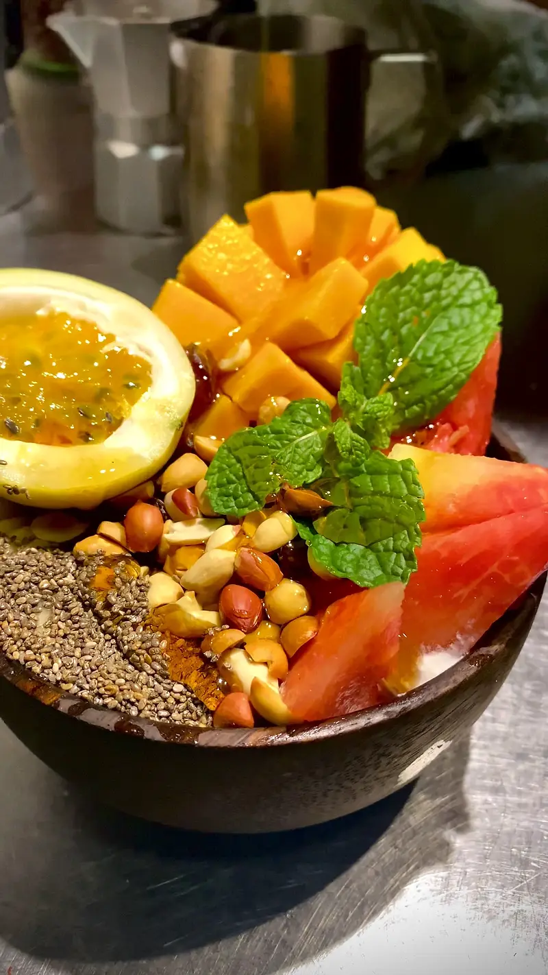 Smoothie bowl topped with fresh mango, passion fruit, watermelon, nuts, seeds and mint