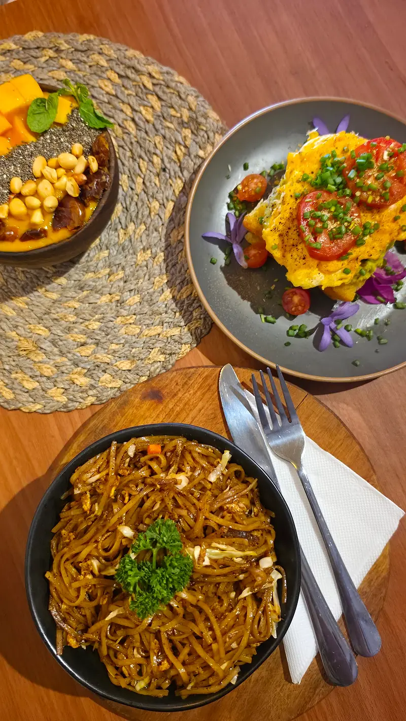 Stir-fried noodles beside an avocado and egg brunch plate and a bowl of chickpeas