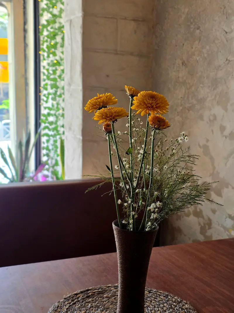 Yellow gerberas in a slim vase on a wooden table by the window